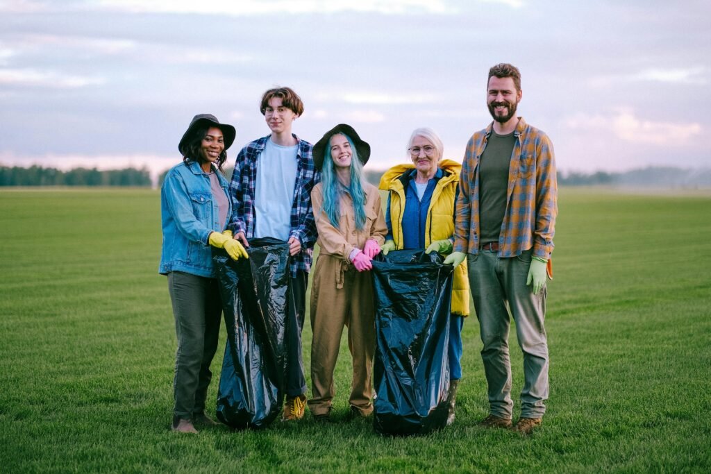 A group of diverse volunteers holding garbage bags while cleaning a green field outdoors.