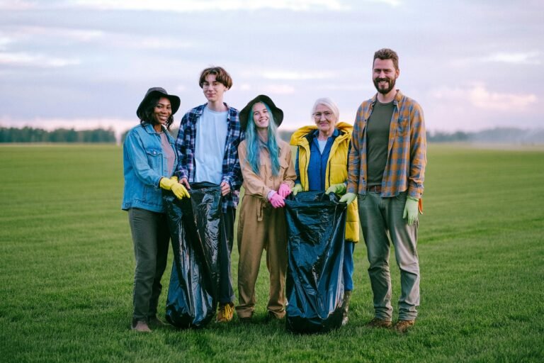 A group of diverse volunteers holding garbage bags while cleaning a green field outdoors.